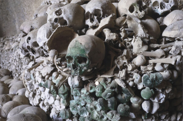 Human skull colored green by lichen moss on a pile of bones at the Cimitero delle Fontanelle ossuary in Napoli Italy.
