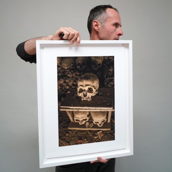 Artist Clayton Porter holding his photograph of a human skull printed with archival pigment ink on rag paper in a white frame.